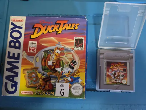 On the left is the original box for Duck Tales on Game Boy, displaying the front cover of the box. On the left is the original Duck Tales game cartridge in a plastic case.