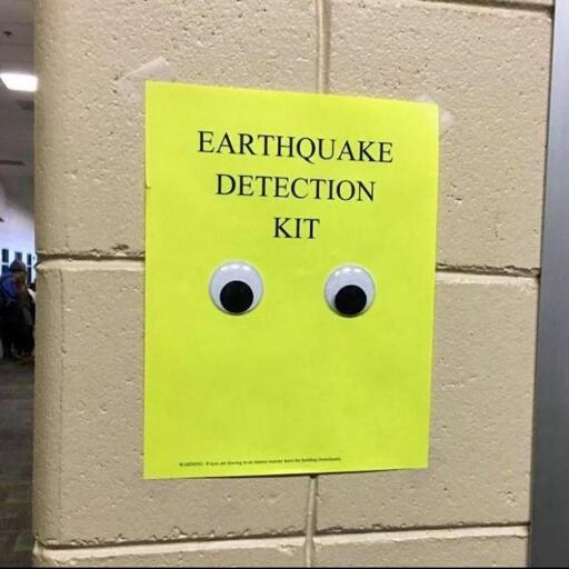 Yellow piece of paper taped to a brick wall. It says "Earthquake detection kit" and has a pair of googly eyes beneath that.