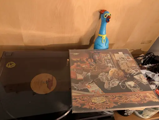 A Frank Zappa and the mothers of invention vinyl playing on a record player, with a blue chicken dog toy in the background. 